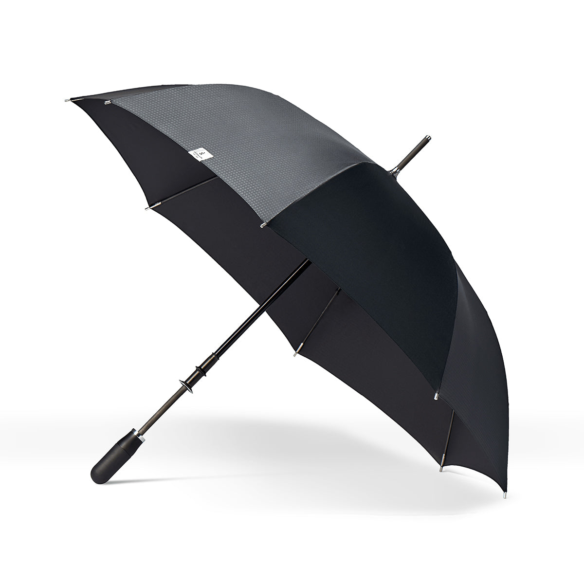 side view of a handmade manual open luxury golf umbrella with a matte black TPR grip handle, Teflon-coated fine denier woven black polyester twill canopy, chrome trim, carbon fiber shaft, fiberglass ribs, and a reflective strap embroidered with “ShedRain Stratus.”