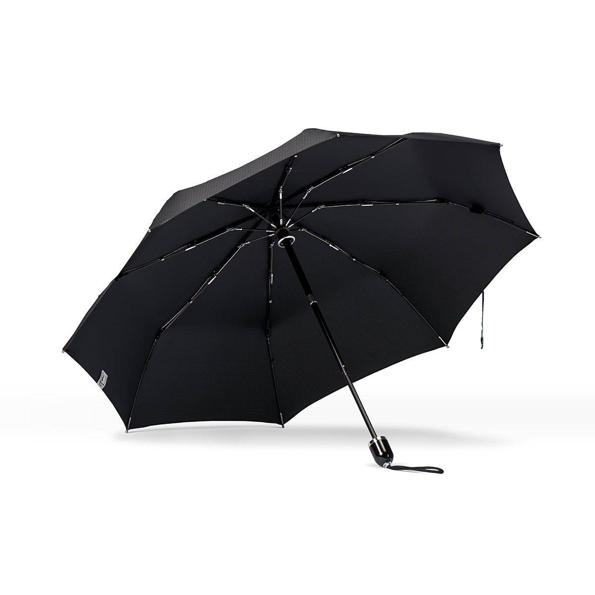underside view of a handmade manual open compact luxury umbrella with a glossy piano finish black handle, detachable waxed cotton wrist strap, Teflon-coated fine denier woven black polyester twill canopy, chrome trim, Trilobe aircraft aluminum shaft, fiberglass ribs, and a reflective strap embroidered with “ShedRain Stratus.”